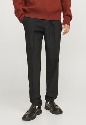 Pantalon noir ajusté en tissu lisse avec une coupe droite et des plis subtils, associé à des mocassins en cuir noir et un pull couleur rouille.