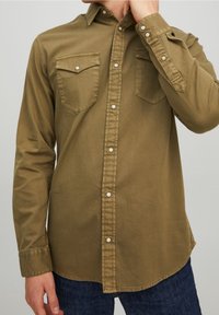 Olivgrünes Hemd mit Knopfverschluss und zwei Brusttaschen, Druckknöpfen und langen Ärmeln. Baumwollmaterial mit glatter Textur, abgerundetem Saum.