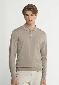 Beige långärmad pikétröja med krage, med knappslå och ribbad kant. Mjuk, slät textur och enkel design.