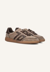 Bruine suède sneakers met gebruinede panelen, donkere veters en een rubberen zool met gum, voorzien van een logo aan de zijkant.