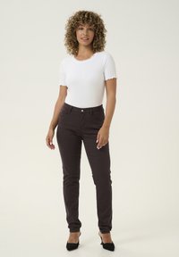 Top bianco a maniche corte con collare scallop, abbinato a pantaloni fitted marrone scuro e scarpe nere con tacco alto.