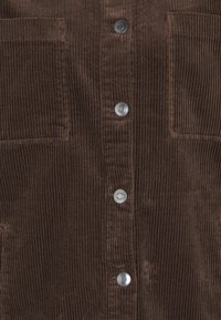 Camisa de corduroy marrón con textura de ribete vertical, botones a presión plateados y dos bolsillos en el pecho para un detalle añadido. Textura suave y diseño estructurado.