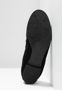 Semelle de chaussure noire avec des motifs de pièces anciennes en relief et le mot "KAISER", indiquant la taille 4½ et la marque "Peter Kaiser" sur fond blanc.