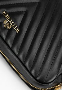Black leather laptop sleeve with quilted pattern, gold logo, and gold zipper. Features smooth texture and precise stitching details.