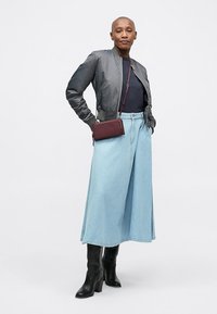 Siva bomberska jakna, mornarsko modra majica, svetlo modra denim krilo, črne škornje do kolen in majhna bordo torbica čez ramo z teksturiranimi detajli.