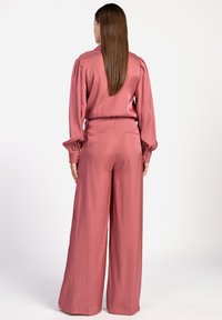 Roze satijnen blouse en wijde broek met een textuurafwerking. De blouse heeft pofmouwen; de broek heeft zijzakken en een comfortabele pasvorm.