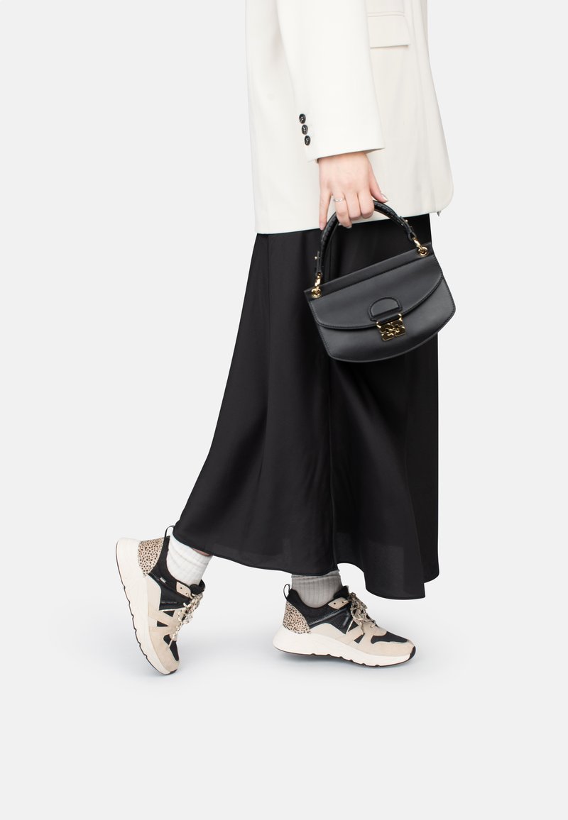 Jupe midi noire associée à des baskets beiges et noires avec un imprimé léopard, et un petit sac à main noir avec des accents dorés.
