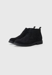 Botines de ante negro con punta redonda, diseño con cordones y tiradores en el talón, que cuentan con una suela de goma texturizada.