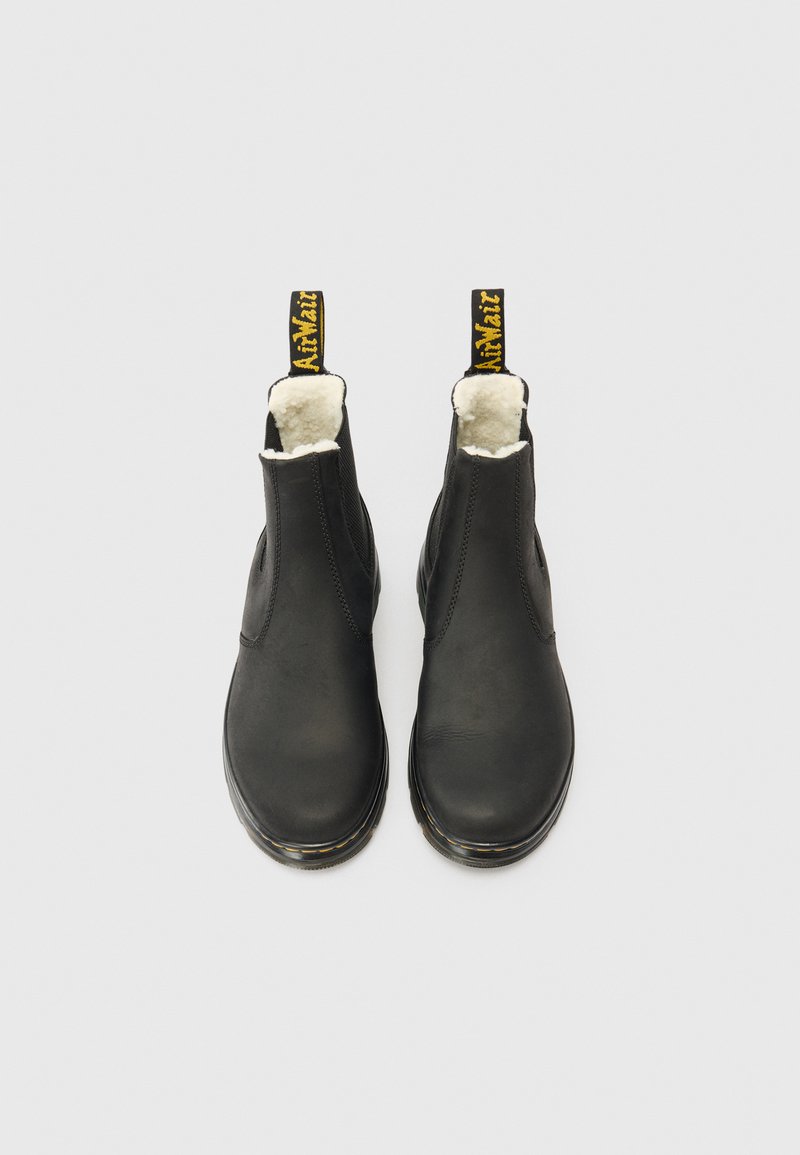 Une paire de bottines noires en cuir avec doublure en polaire blanche et tirants noirs portant un texte jaune, présentées de dessus sur un fond blanc.