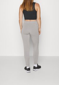 Pantalones joggers ajustados en gris con una textura suave, piernas ajustadas y una cinturilla alta. Combinados con zapatillas deportivas negras y un top corto negro.