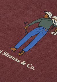 Textil color marrón con una ilustración de una figura vestida con una camisa gris y jeans azules, sosteniendo una llave inglesa, con el texto "Levi Strauss & Co." debajo.