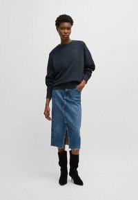 Navy sweatshirt with dropped shoulders, paired with a high-waisted denim skirt featuring a front slit and frayed hem. Black knee-high boots.