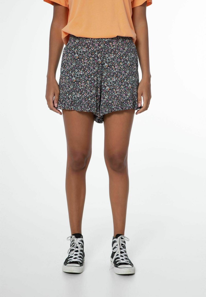 Svarta shorts med ett färgglatt blommönster, med en bekväm passform och fransad nederkant. Matchas med en lös orange t-shirt och svarta sneakers.