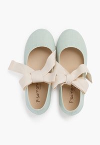 Ballerines en toile vert clair avec une texture douce, dotées d'un ruban en tissu beige noué à l'avant et d'un logo sur la semelle intérieure marron.