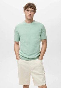 Pulover scurt cu mânecă scurtă de culoare verde deschis, cu guler rotund, asortat cu pantaloni scurți crem. Ambele articole au texturi netede și o croială lejeră.