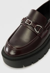 Burgundi värvi nahast loafersid paksu musta platvormpõhjaga, dekoratiivse hõbedase pandlaga ja kontrastsete punaste õmblustega servade ümber.