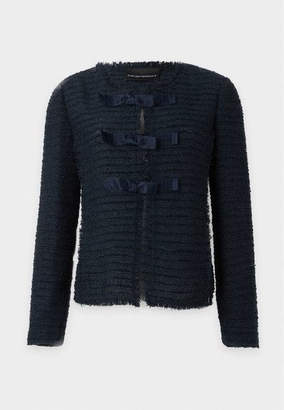 Veste bleu marine texturée à manches longues, col rond et trois fermetures devant avec nœuds en ruban, sans poches ni boutons visibles, fond uni.