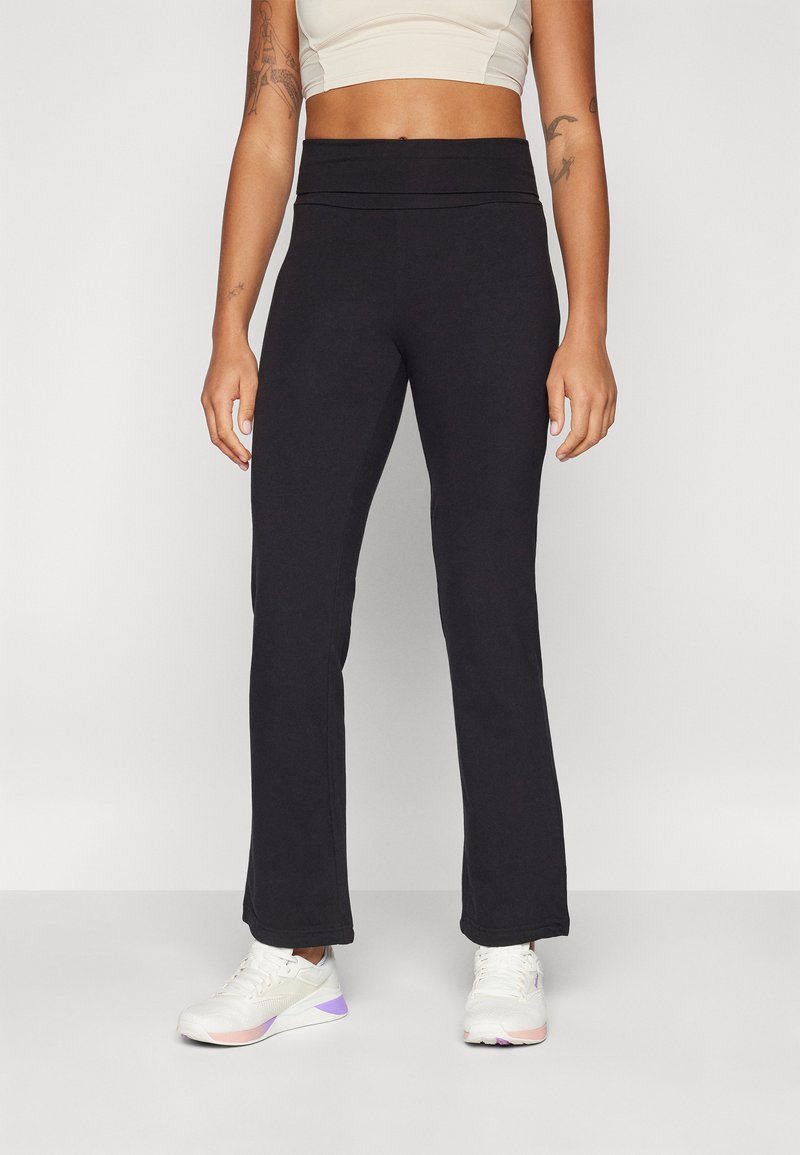 Pantaloni sportivi neri con design a campana, caratterizzati da una cintura larga e una texture liscia, abbinati a sneaker bianche con accenti pastello.