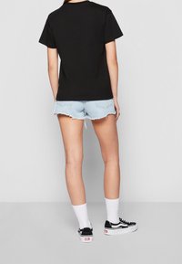 T-shirt en coton noir à manches courtes, associé à un short en jean léger effiloché, des chaussettes blanches, et des baskets noires avec des semelles blanches.