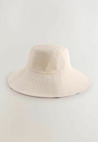 Beige bucket hat met een brede rand, gemaakt van gestructureerde stof, heeft een vlakke kroon en subtiele naaddetails langs de rand.