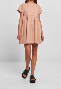 Kurzes pinkes Baumwollkleid mit Rundhalsausschnitt, kurzen Ärmeln und geraffter Taille. Kombiniert mit schwarzen Slipper-Sandalen. Einfacher, lässiger Schnitt.