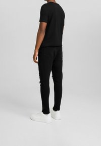 Svart t-shirt med kort ärm och rund halsringning, kombinerad med slitna svarta jeans. Vita sneakers fulländar outfiten.