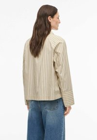 Veste à rayures beige avec une coupe décontractée, manches longues et poignets boutonnés, associée à un jean bleu à jambes larges. Design simple et décontracté.