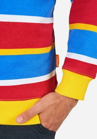 Sudadera de rayas multicolores con rayas horizontales en azul, rojo, amarillo y blanco. Puños amarillos acanalados, con una etiqueta de marca visible.