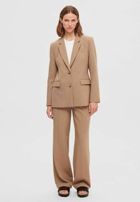 Beige skræddersyet blazer med to knapper og for- lommer, parret med brede bukser i matchende stil. Stoffet ser glat og tekstureret ud.