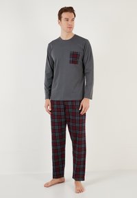 Camiseta gris de manga larga con un bolsillo a cuadros rojo y negro, combinada con pantalones de pijama a cuadros en tonos rojo, negro y gris. Tela ligera.