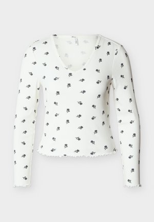 Λευκή ριμπ μακρυμάνικη μπλούζα με V-λαιμόκοψη και μικρά μαύρα λουλουδένια σχέδια, με τελειώματα στις άκρες μύγες στα μανίκια και στο κάτω μέρος.