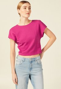 Fuchsia kurzes T-Shirt mit strukturiertem Muster, Rundhalsausschnitt und kurzen Ärmeln, kombiniert mit hellblauen Jeans.