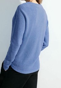 Sininen teksturoitu neulepusero, jossa on pyöreä kaula-aukko, pitkät hihat ja kaareva helma. Päällä mustat housut, takakuvassa.