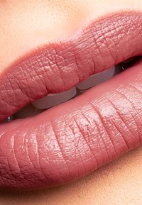 Volle, matte lippen in een zachte roze tint, met een gladde textuur en gedefinieerde contour, tegen een perzikachtige achtergrond.