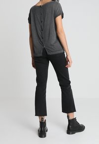 Top gris de manga corta con cierre de botones en la parte posterior, combinado con unos jeans negros cortos y botas negras hasta el tobillo con suela gruesa.