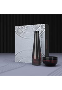 Bottiglia di shampoo nera e contenitore rotondo esposti con una scatola bianca testurizzata, caratterizzata da motivi curvi e testo rosso su uno sfondo neutro.