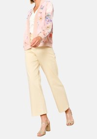 Ljusrosa blommig bomberjacka med genomskinligt tyg, beige vida byxor och sandaler med guldblockklack. Jackan har en solid ribbad nederkant.