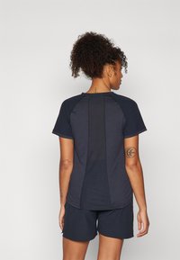 Marineblå treningstrøye med korte ermer og mesh-panel bak, sammen med marineblå shorts. Har stretchmateriale og kontrasterende sømmer.