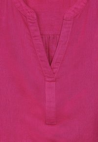 Blusa di lino fucsia con scollatura a V, caratterizzata da una piega sotto il collo e dettagli cuciti lungo i bordi.