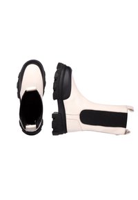 Botas de tobillo de imitación de piel blanca con una suela de goma negra gruesa, paneles elásticos laterales y una textura suave. Presenta una puntera redondeada.