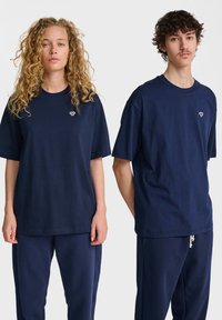 Marinblå bomulls t-shirts med korta ärmar, med en liten broderad design på bröstet, i kombination med matchande marinblå byxor.