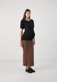 Top negru cu dungi, cu manșoane scurte tip puff, purtat cu o fustă maxi maro, tot cu dungi. Încălțămintea este formată din pantofi slip-on negri.