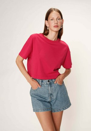 T-shirt cropped rose vif à manches courtes, associé à un short en denim taille haute. Le tissu semble lisse et décontracté.