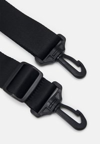 Cinghia nera in nylon con hardware regolabile e ganci in plastica a entrambe le estremità. La superficie presenta un aspetto tessuto e testurizzato.