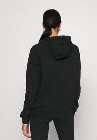 Svart hooded sweatshirt i mjukt, texturerat tyg. Har raglanärmar och en framsidig känguruficka. Bakifrån visas en avslappnad passform.