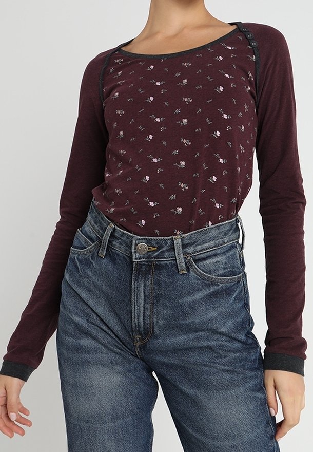 Maroon långärmad topp med blommönster, svart piping och knappdetaljer; matchad med högmidjade blå denimjeans.