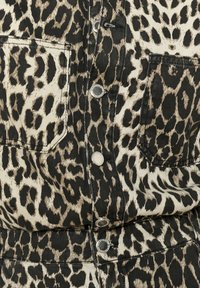 Chaqueta de mezclilla con estampado de leopardo en colores negro y beige, dos bolsillos frontales y botones a presión plateados. Tejido texturizado con patrones distintos.