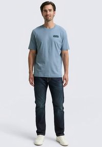 Világoskék pamut rövid ujjú póló mellkasi grafikával, sötét farmernadrággal és fehér tornacipővel párosítva. Egyszerű és laza dizájn.