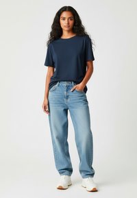 T-shirt bleu marine à col rond associé à un jean bleu clair ample. Baskets blanches, texture lisse, design décontracté et coupe droite.