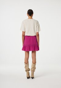 Lichtbeige korte mouwen top en een knielange roze geplooide rok met een gerimpelde zoom. Gecombineerd met beige laarzen tot de knie.